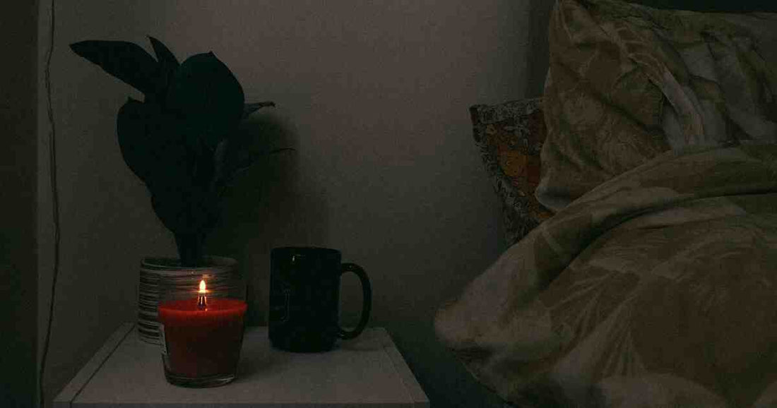 cozy bedside table with a lit scented candle potted plant and mug for calming private space