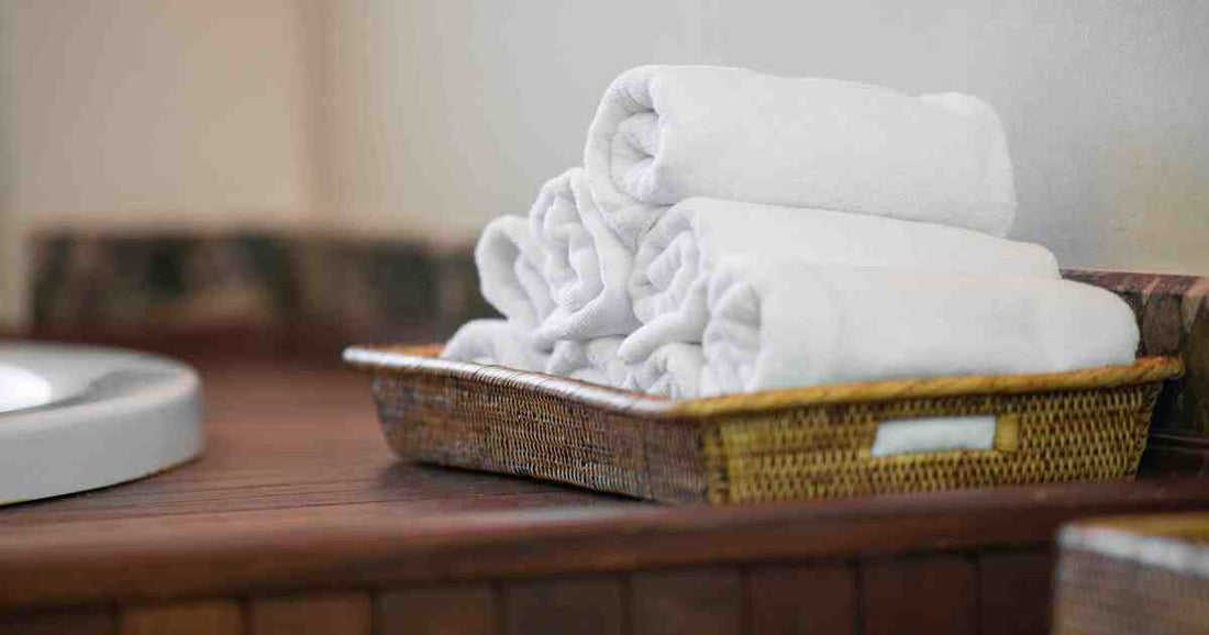 fresh rolled white clean towels in a woven basket on a wooden bathroom vanity representing hygiene care and item replacement standards