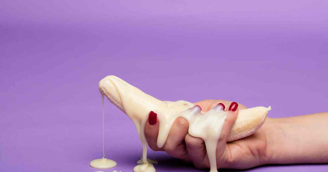 hand holding a smooth banana covered in flowing creamy texture over purple background